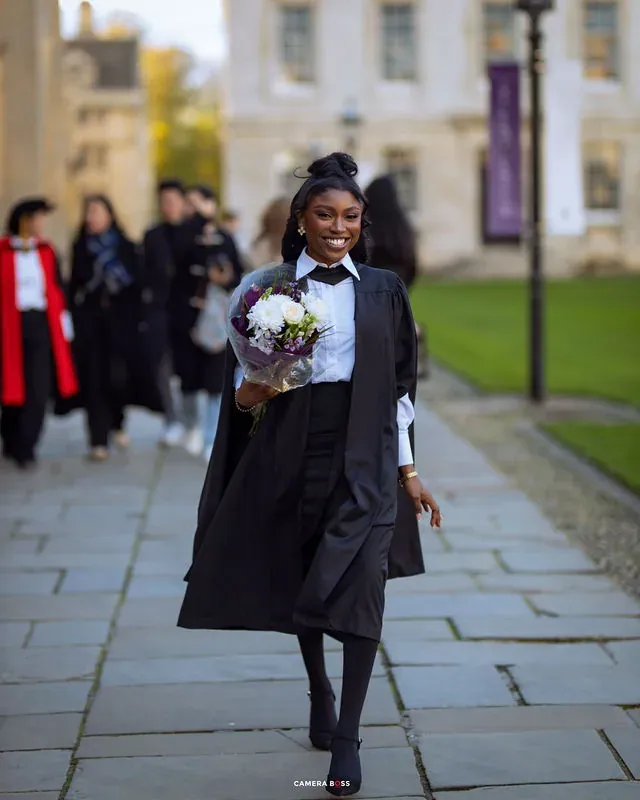 A graduate walking with a bouquet in a black academic gown. CameraBoss portfolio: Peters Grad.