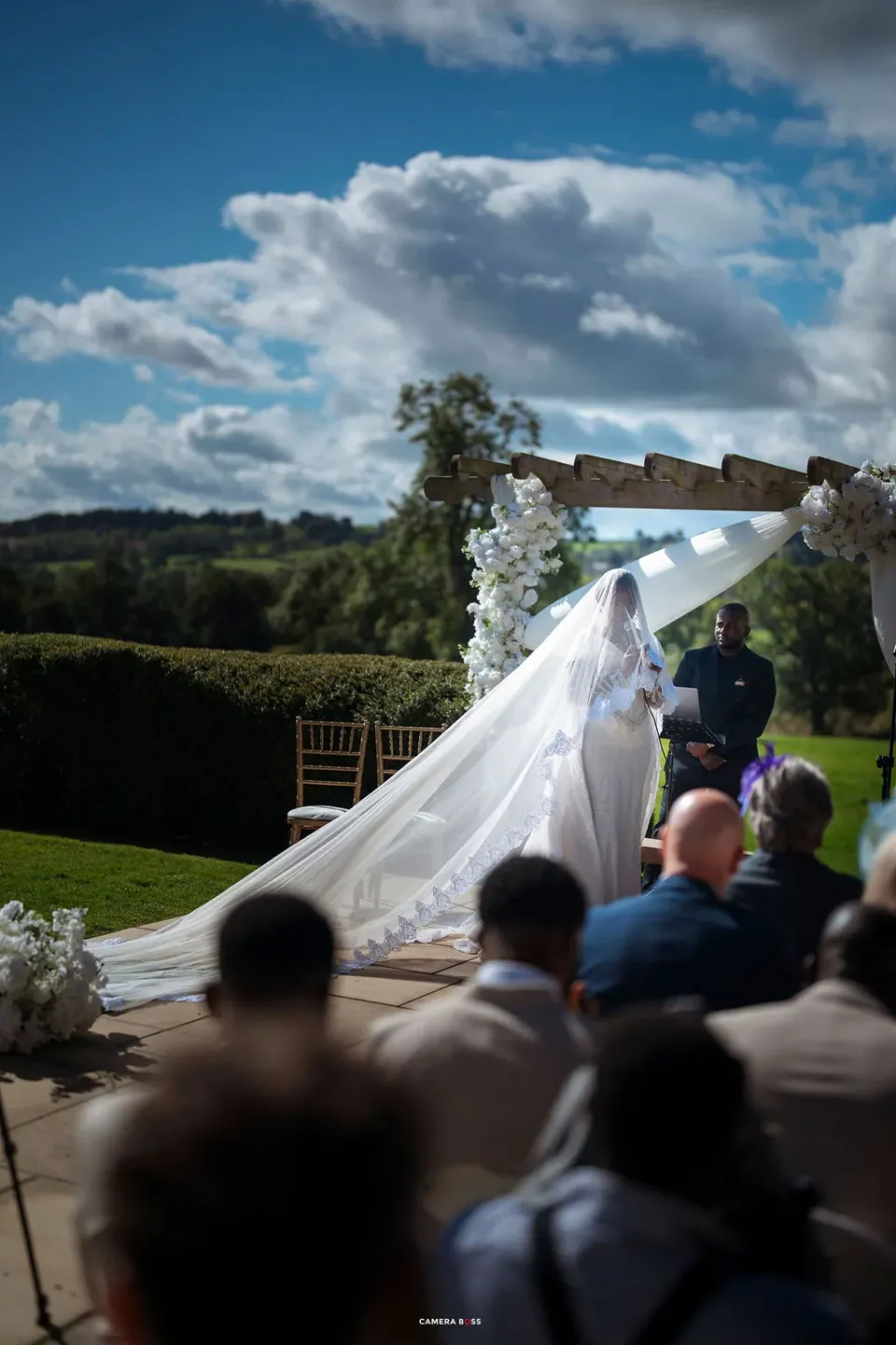 Helen's long veil beneath the flower-dressed pergola during the outdoor ceremony at Shottle Hall