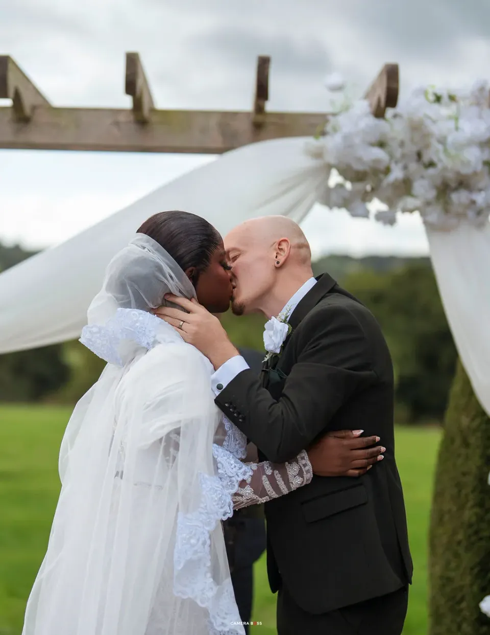 Helen and Jack kissing beneath the flower-dressed pergola at Shottle Hall