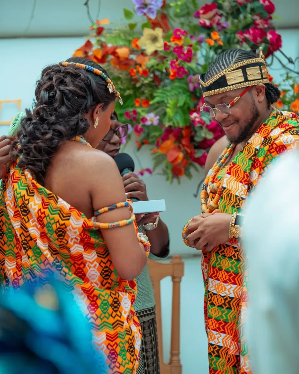 Deacon Famous and Faith facing each other in orange and green kente wedding attire