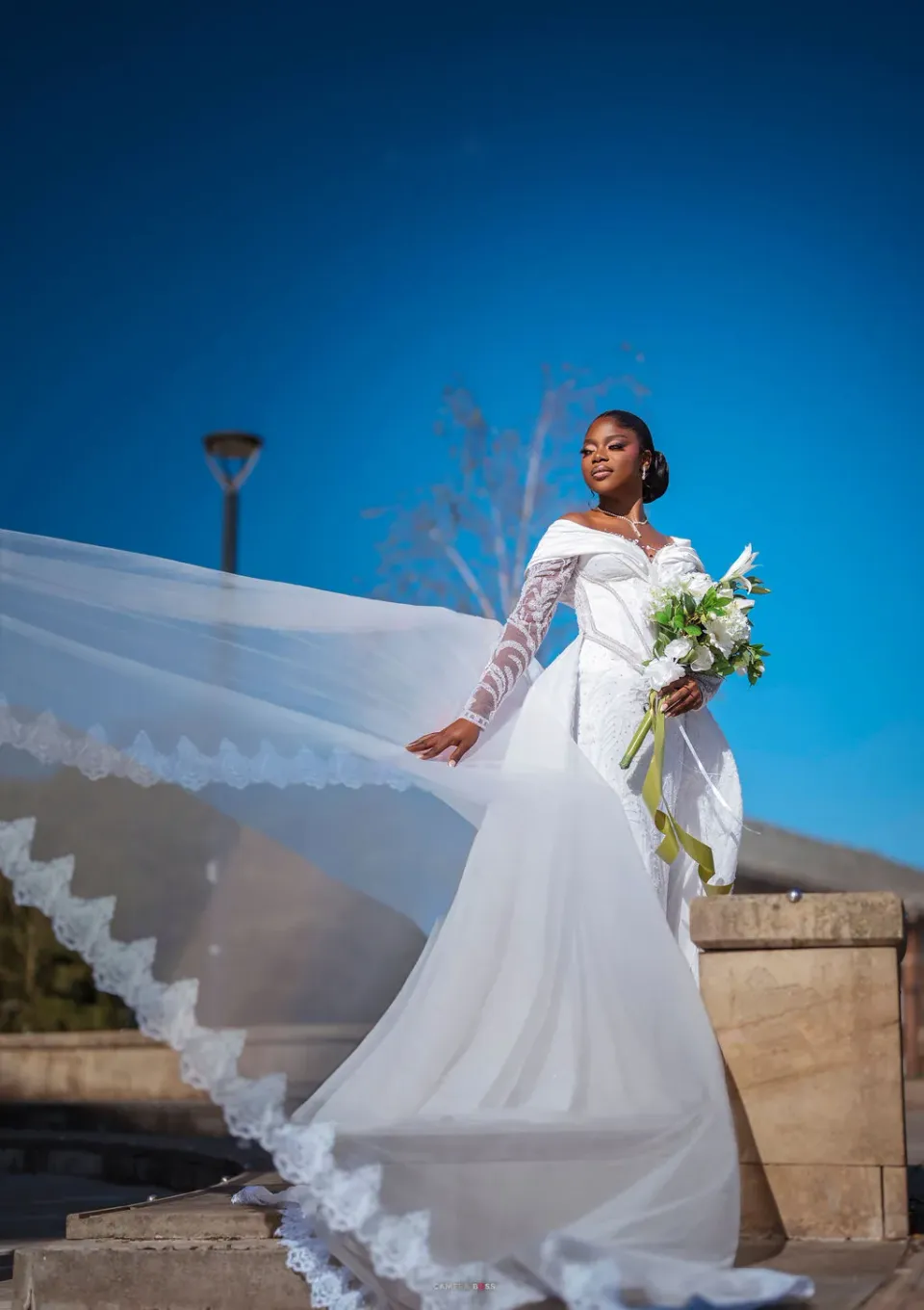 Helen holding her bouquet with her long lace-edged veil lifted out beside her
