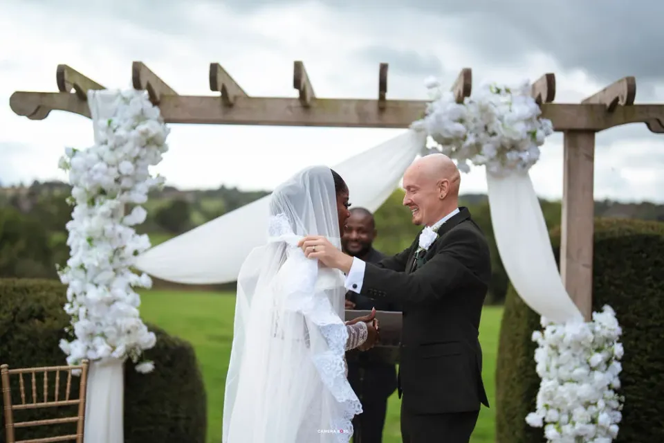 Jack lifting Helen's veil beneath the white flowers at Shottle Hall