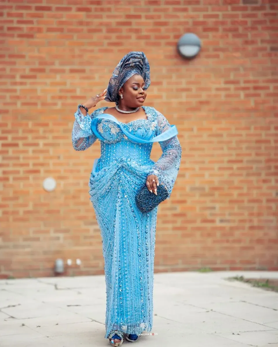Elegant turquoise blue lace gown with long bell sleeves and sequin details stands out against rustic brick wall backdrop.