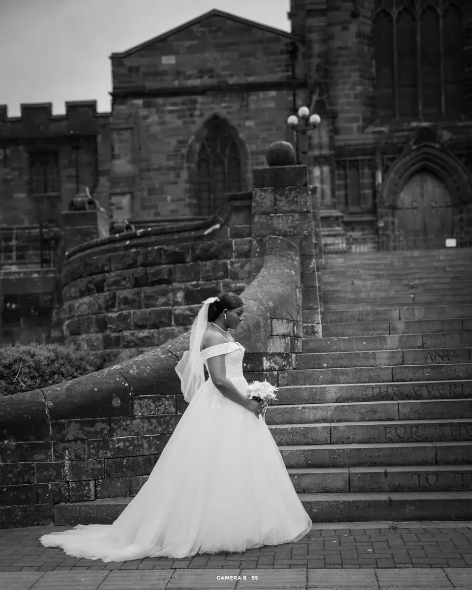 A bride in a flowing white ballgown wedding dress stands on historic stone steps of a gothic church.