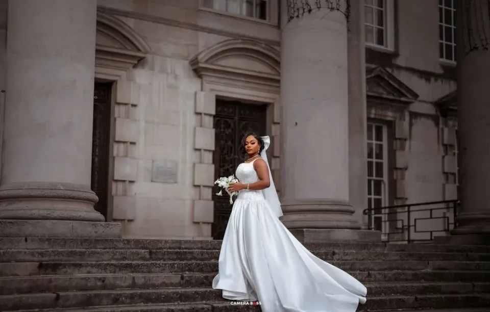 Bride in flowing white dress twirls gracefully on stone steps of historic building during wedding photoshoot.
