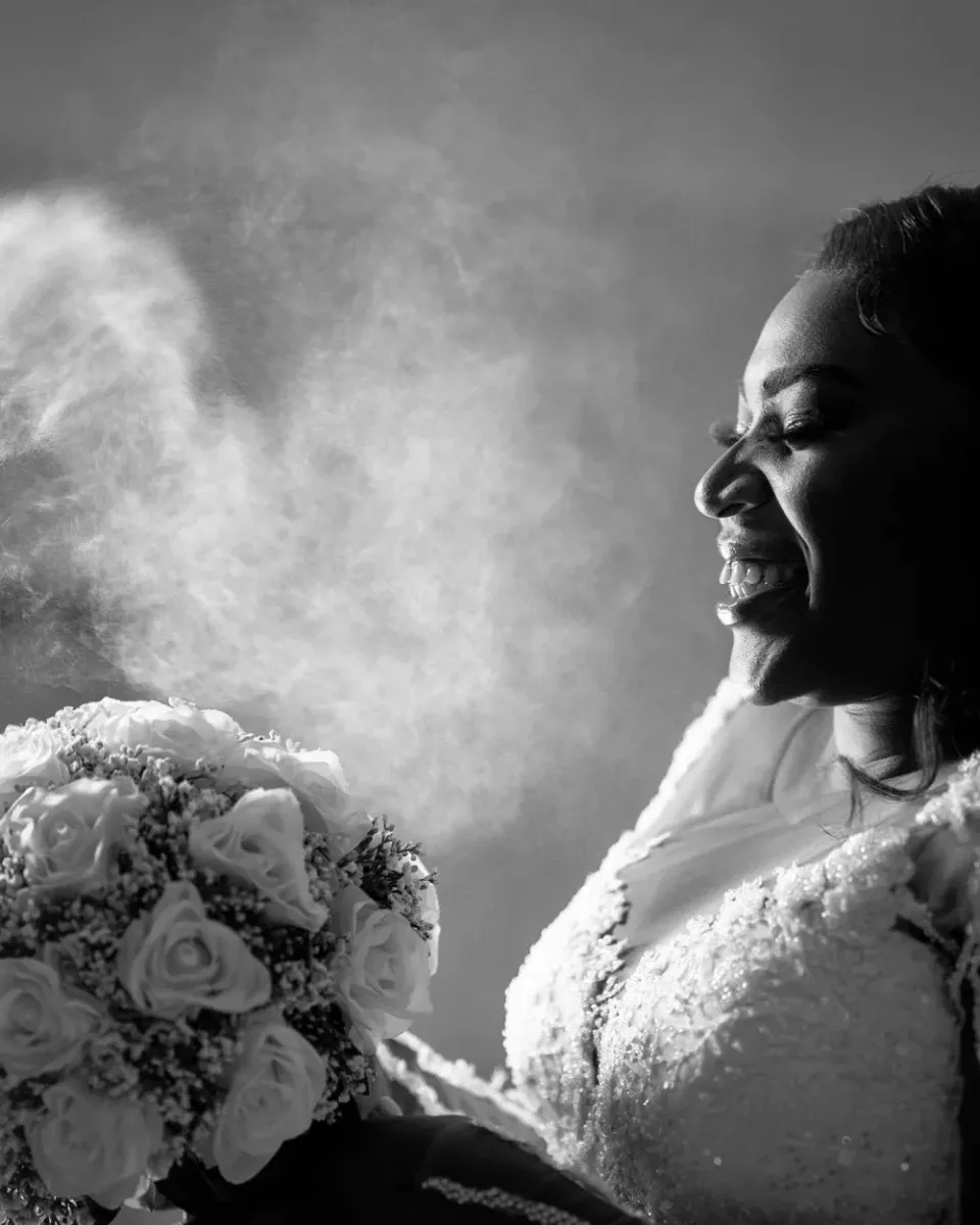 A joyful bride laughs while holding a white rose bouquet in an artistic black and white portrait.